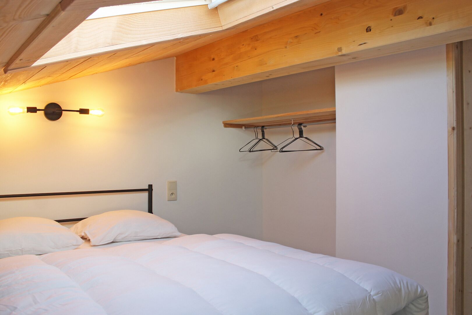 A bedroom with a bed, a wall-mounted light, and a wooden ceiling.