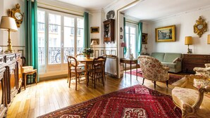Un salon spacieux comprenant un coin repas, un canapé vert et un tapis rouge à motifs.