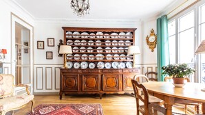 Une salle à manger avec une table en bois, des chaises, un tapis rouge à motifs, un buffet contenant de la vaisselle et un lustre.