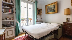 Une chambre à coucher avec un lit, une bibliothèque, une commode, une lampe et un tableau accroché au mur.