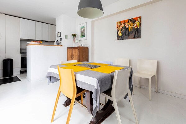 A modern kitchen with white cabinets, a dining area with a table set for four, and a painting on the wall.