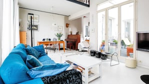 A modern living room with a blue sofa, a white coffee table, and a dining area with a wooden table and chairs. - White House, by Veeve (Paris)