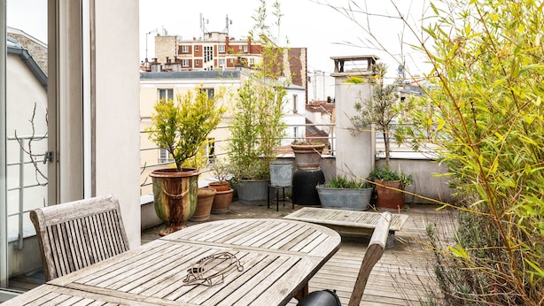 A rooftop terrace with wooden tables and chairs, potted plants, and a view of surrounding buildings. - White House, by Veeve (Paris)