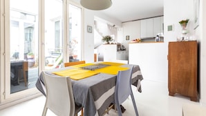A dining area with a table set for four, a kitchen in the background, and a sliding glass door leading to an outdoor space. - White House, by Veeve (Paris)
