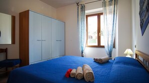 A bedroom with a large bed, a wardrobe, a chair, and a window with curtains. - Rena Bianca Apartment, 40 meters from the beach, No. DAR-T5 (Santa Teresa Gallura)