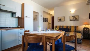 A compact kitchen with a dining table and chairs, a sofa, and a small side table with a lamp. - Rena Bianca Apartment 40m from the beach No. DAR-T5 (Santa Teresa Gallura)