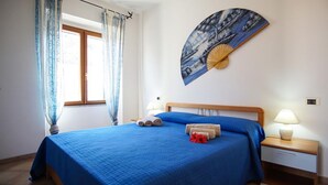 A bedroom with a large bed, two bedside tables, a window with curtains, and a wall-mounted fan. - Rena Bianca Apartment 40m from the beach No. DAR-T5 (Santa Teresa Gallura)
