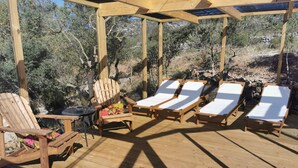 Eine Holzterrasse mit Liegestühlen und einem Tisch, umgeben von Natur.