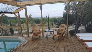 Eine Holzterrasse mit zwei Adirondack-Stühlen und einem kleinen Tisch, mit Blick auf einen Pool und eine reizvolle Landschaft.
