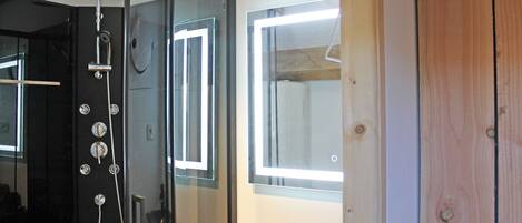 A bathroom with a glass shower enclosure, a sink, and a window.