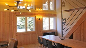 Un interior de madera con una mesa de comedor, sillas, una araña y ventanas amplias.