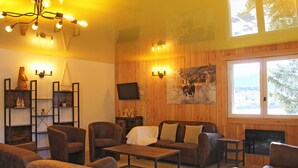 Una sala de estar acogedora con paredes de madera, una chimenea y un ventanal grande. Hay varias zonas de estar con sofás y sillones.