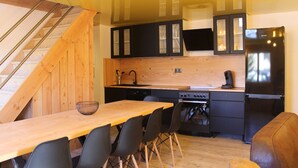 Una cocina moderna con armarios de madera, un refrigerador negro y un comedor con mesa y sillas de madera.