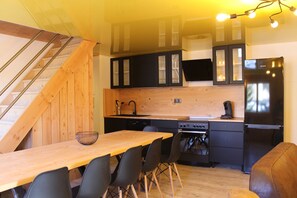Cozinha moderna com armários de madeira, geladeira preta e área de refeições com mesa e cadeiras de madeira.