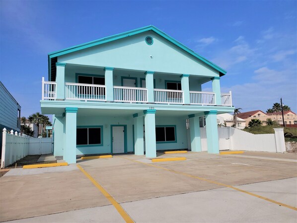A two-story building with a light blue exterior, a balcony on the upper floor, and a parking lot in front.