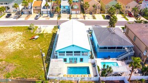 A two-story building with a swimming pool, surrounded by palm trees and other residential buildings. - Lantana Retreat 3 - Spacious 3BR w/ Pool (South Padre Island)