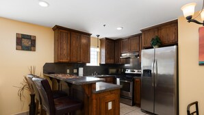 A kitchen with wooden cabinets, a stainless steel refrigerator, a microwave, and a bar area with stools. - Lantana Retreat 3 - Spacious 3BR w/ Pool (South Padre Island)