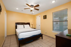 A bedroom with a bed, a ceiling fan, a nightstand, a lamp, a door, and a window with blinds.