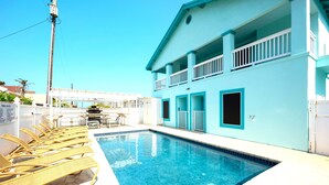 A swimming pool with lounge chairs, a two-story building with balconies, and a clear blue sky. - Lantana Retreat 3 - Spacious 3BR w/ Pool (South Padre Island)