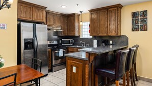 A kitchen with wooden cabinets, stainless steel appliances, a granite countertop, and bar stools.