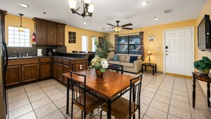 A kitchen with wooden cabinets, a dining table with chairs, a ceiling fan, and a large window.