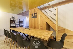 A wooden dining table with chairs, a staircase, and a wall with a tree silhouette. - Apartment La Chouette  (Formiguères)