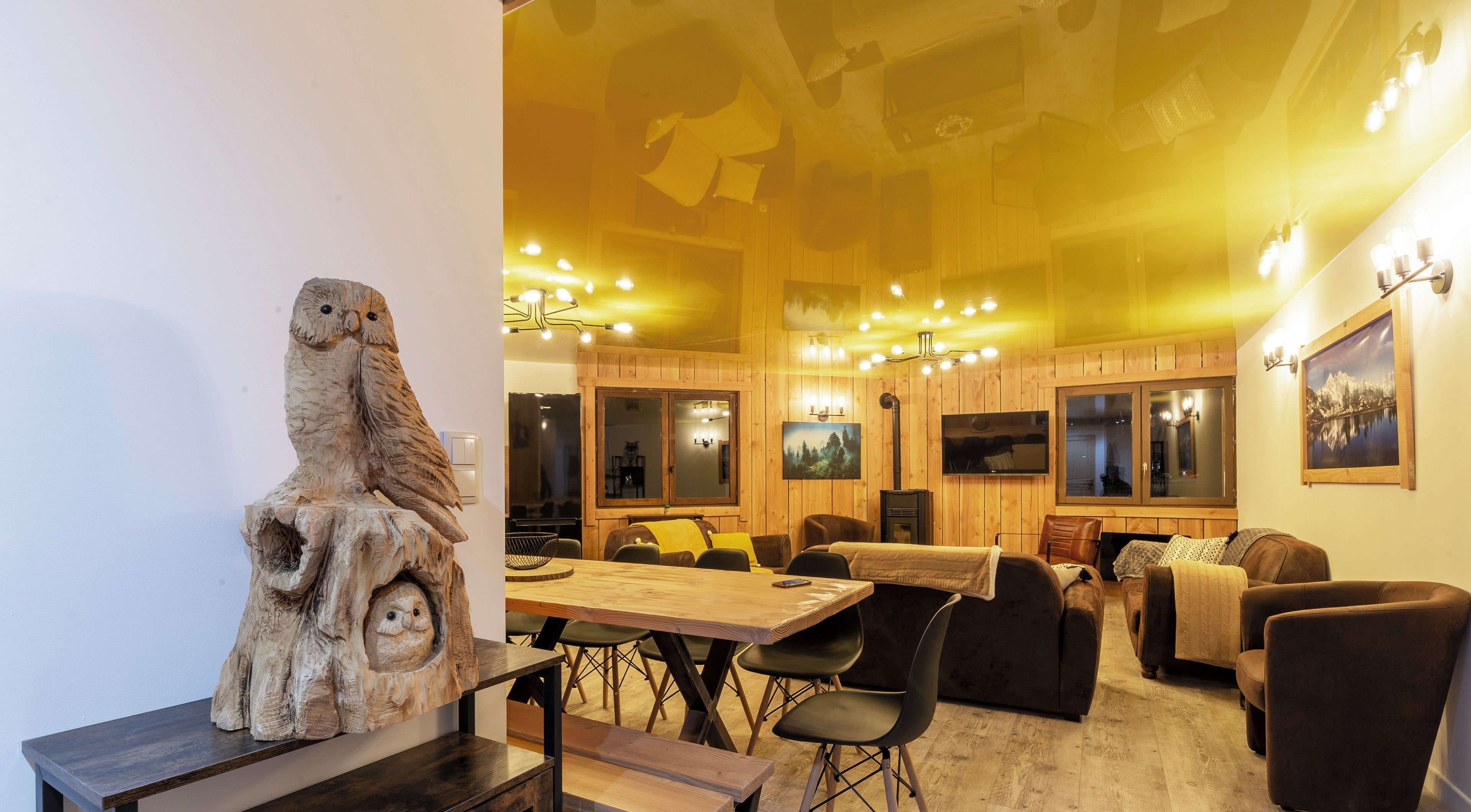 Une pièce chaleureuse et bien éclairée, avec une table à manger en bois, des sièges confortables et une sculpture rustique en bois.