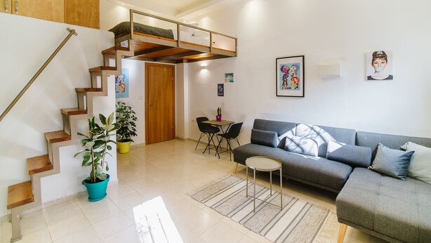 A modern living room with a staircase, a sofa, a dining table, and a potted plant. - Bugrashov Beach Studios (Tel Aviv)