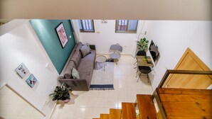 A spacious living area with a sofa, a small table, and a staircase. - Bugrashov Beach Studios (Tel Aviv)