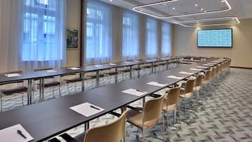 A conference room with a long table, chairs, a projector screen, and large windows with curtains.
