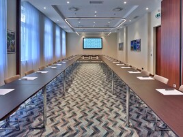 A conference room with a long table, chairs, a projector screen, and a patterned carpet.