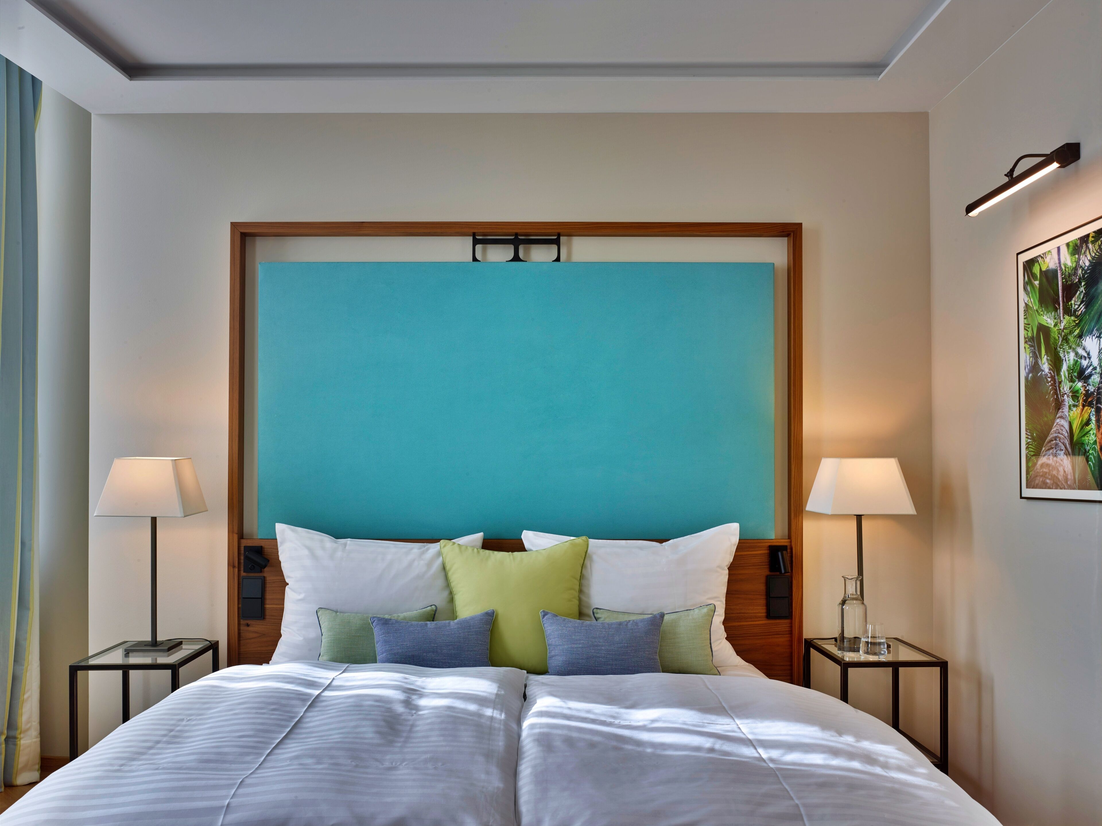 Une chambre d’hôtel avec un grand lit, deux tables de chevet, une tête de lit et une lampe fixée au mur.