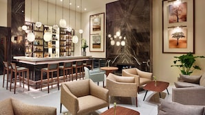 Zona de bar moderna con pared de mármol, luces colgantes y chimenea. Hay sofás y sillones dispuestos alrededor de una mesa central.