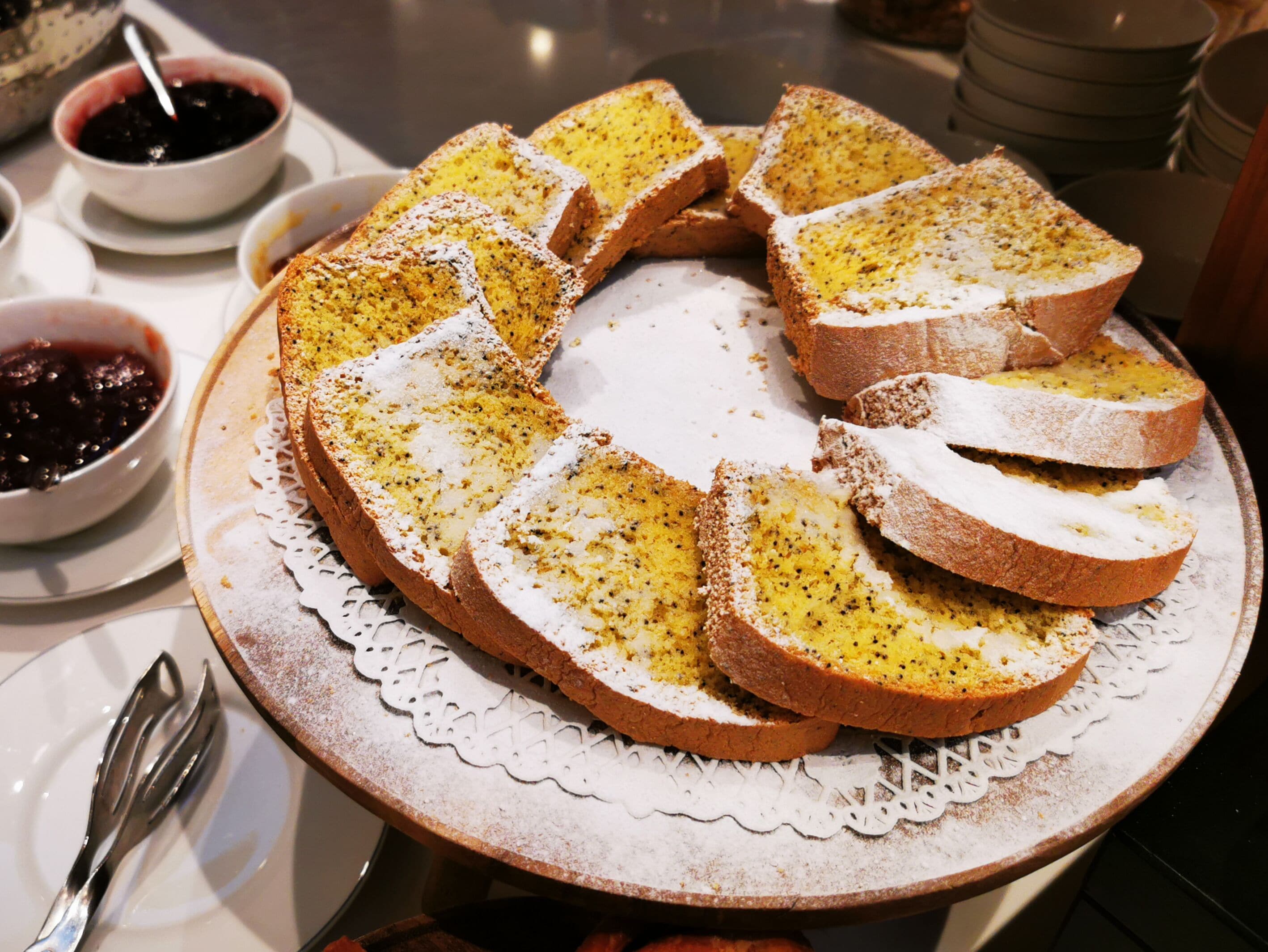A round table with a white lace doily, a plate of sliced bread with a white topping, and two bowls of jam.
