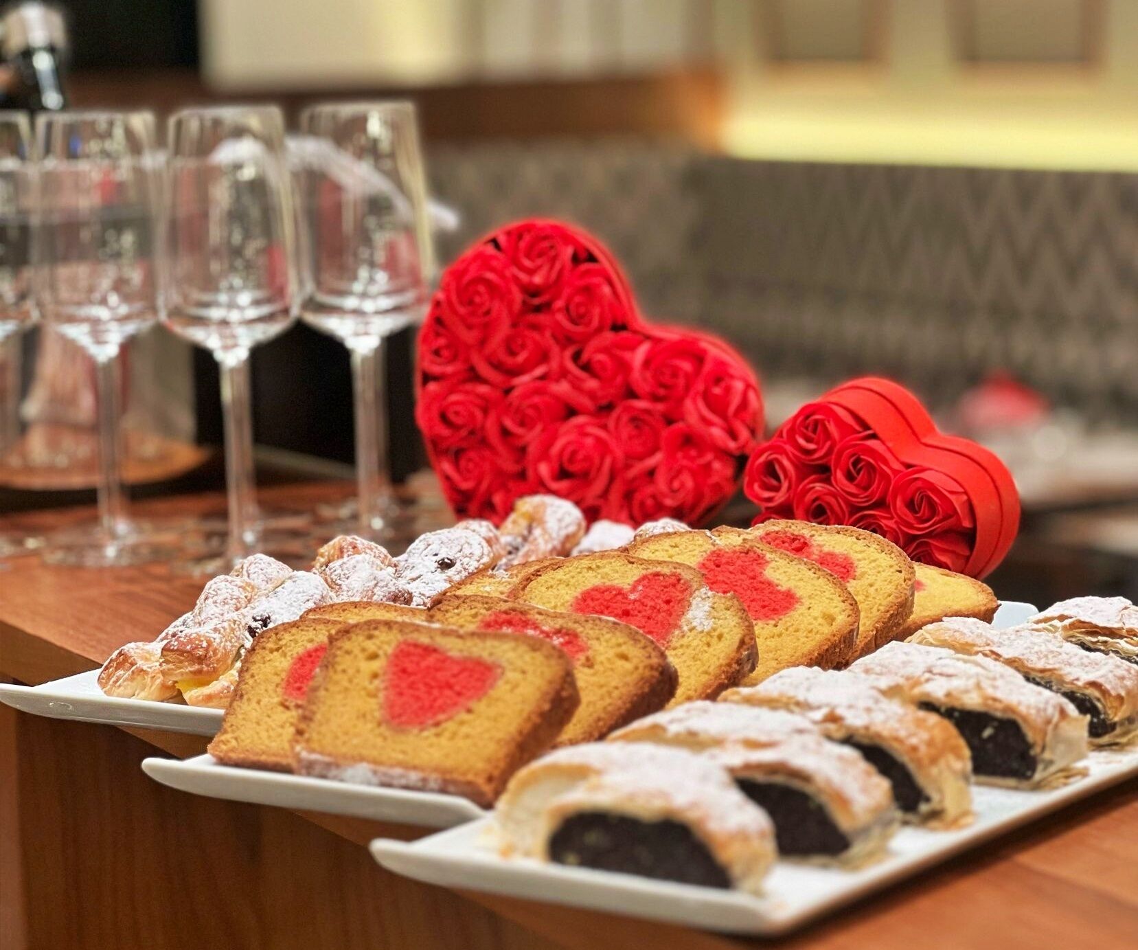 Una mesa con pasteles, vasos y rosales rojos decorativos.