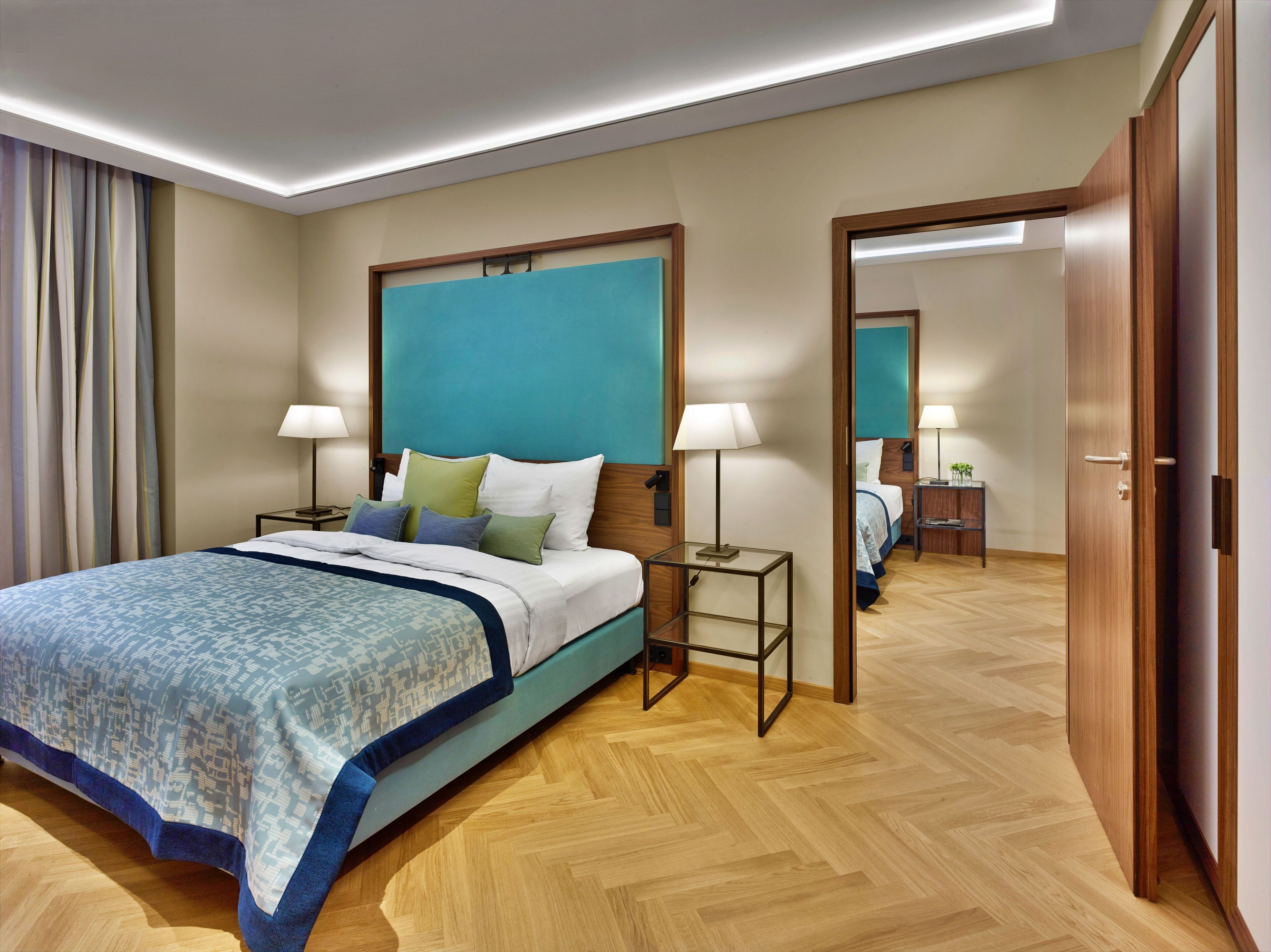 Habitación de hotel con una cama grande, mesitas de noche con lámparas, un espejo y suelo de madera.