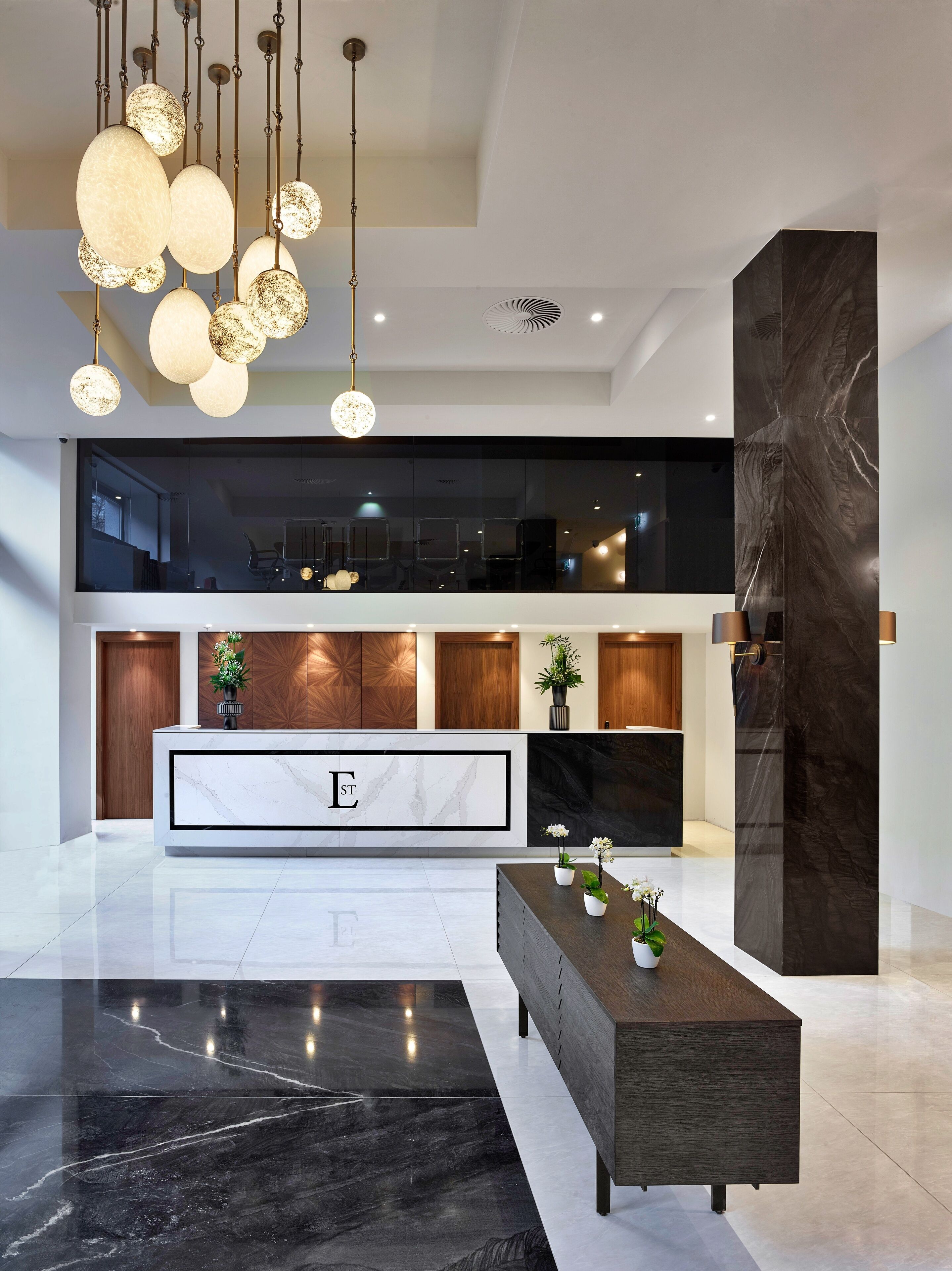 Een modern interieur met een marmeren receptiebalie, een zwart-wit marmeren vloer en een grote, donkere marmeren kolom.