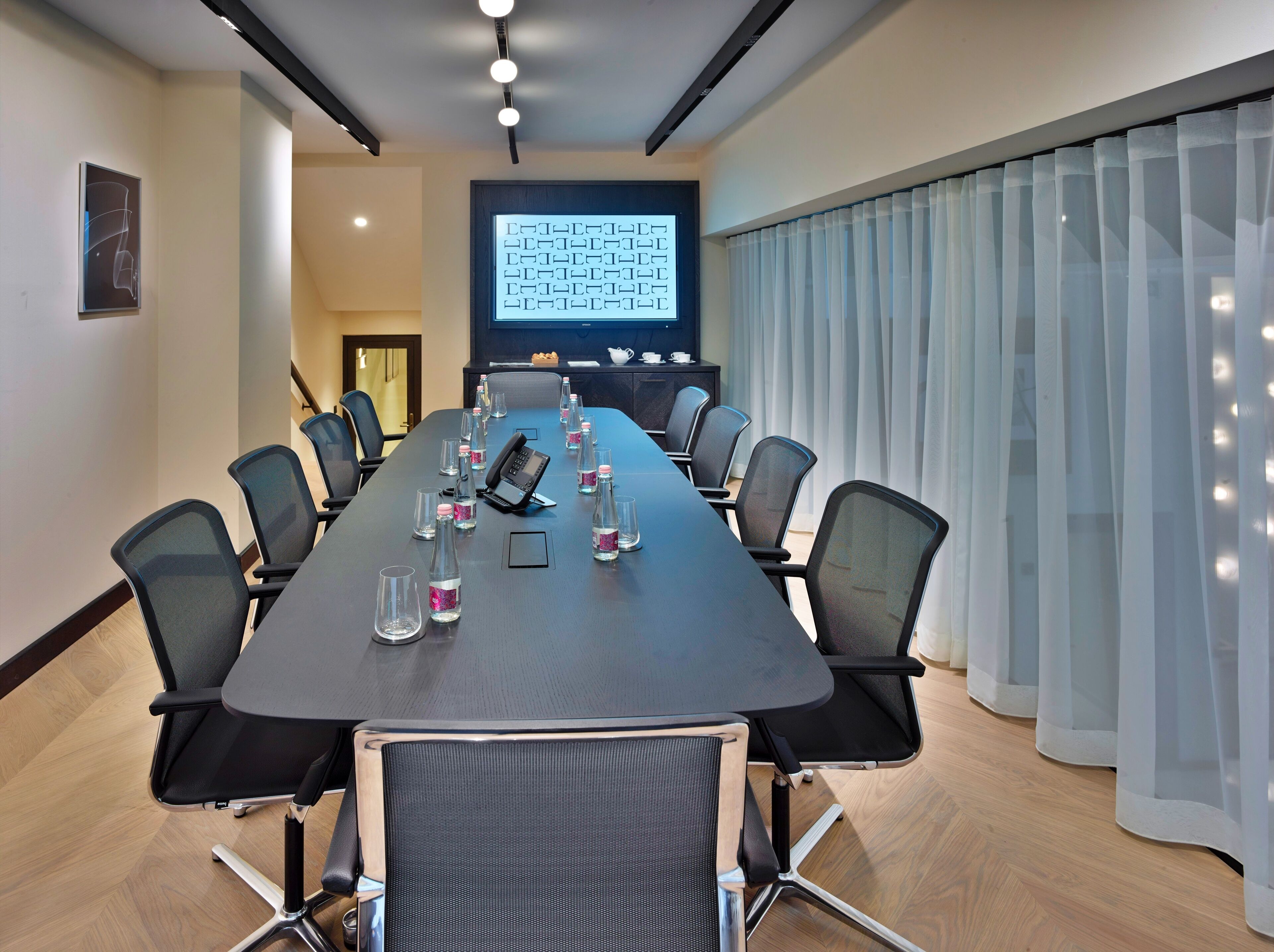 Un salón de conferencias con una larga mesa, sillas, una pantalla de proyector y una estación de café.