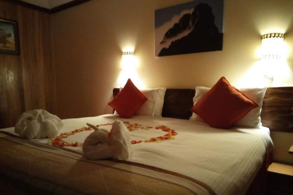 A hotel room with a neatly made bed, red pillows, and a bouquet of flowers on the bed.