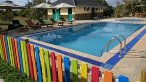 A swimming pool with a blue border, surrounded by colorful wooden fences and lounge chairs. - The Nelion (Naro Moru)