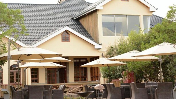 A building with a tiled roof, outdoor seating with umbrellas, and a small pool. - The Nelion (Naro Moru)