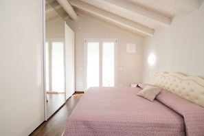 A bedroom with a large bed, a wooden ceiling, and a door leading to another room.