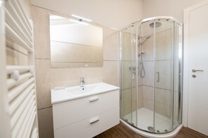 A modern bathroom with a glass-enclosed shower, a white sink, and a large mirror.