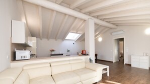 Un salon moderne avec un canapé blanc, un coin cuisine doté de meubles blancs et une lucarne.