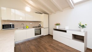 Une cuisine moderne avec des meubles blancs, un four à micro-ondes, un évier et une cuisinière. Le sol est en bois et une lucarne se trouve au-dessus de la cuisine.