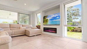 A spacious living room with a beige sectional sofa, a flat-screen TV mounted on the wall, and a fireplace.
