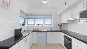 Eine moderne Küche mit weißen Schränken, schwarzen Arbeitsplatten, einem Geschirrspüler und einem Fenster mit Meerblick.