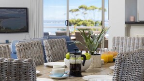 Ein Essbereich mit Korbmöbeln, einer Kaffeemaschine, einem Topfpflanzen und Blick aufs Meer.