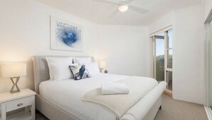 Ein Schlafzimmer mit einem Bett, Nachttischen, einem Deckenventilator, einem Fenster und einem Wandbild.