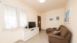 A living room with a brown sofa, a white entertainment unit, and a television. - Appartamento Lilli (Manerba del Garda)
